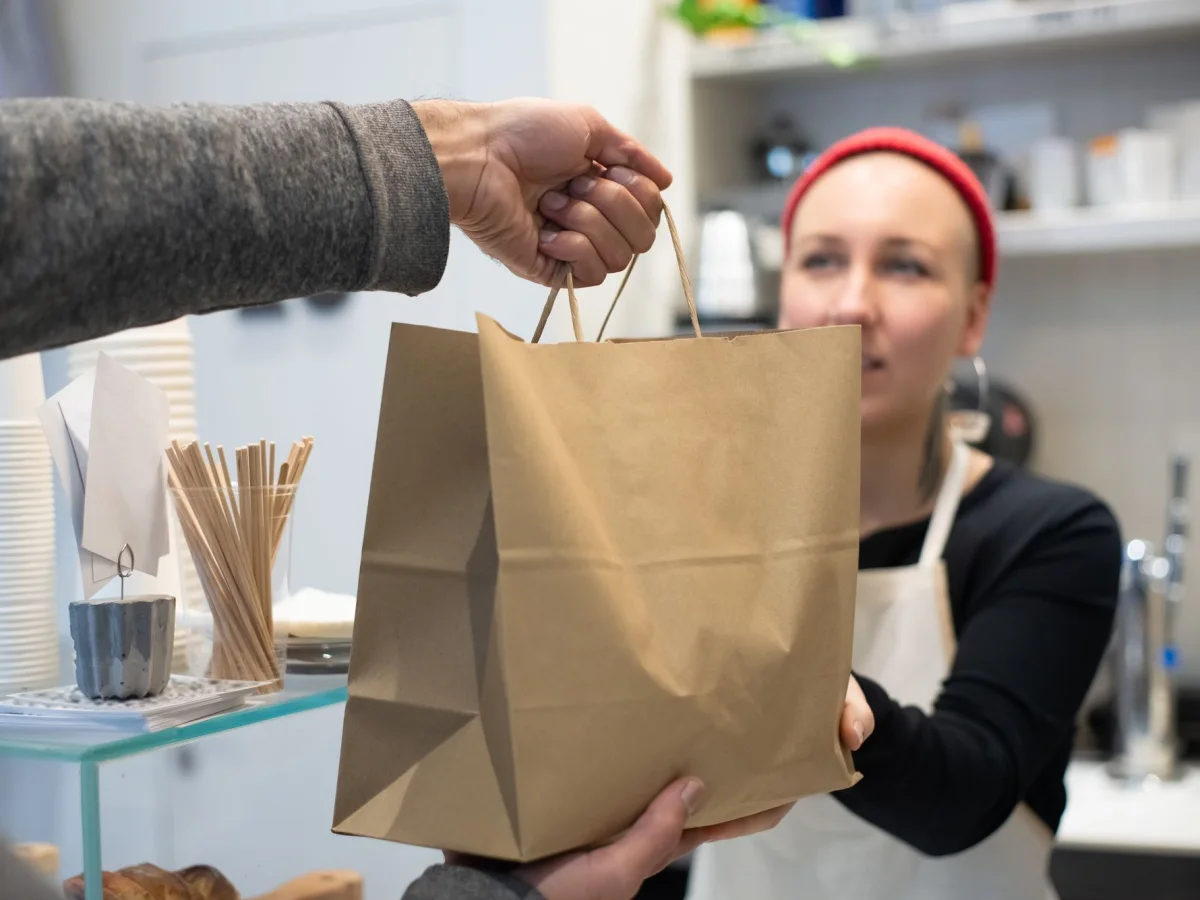 A shop worker handing a paper pickup bag to a customer
